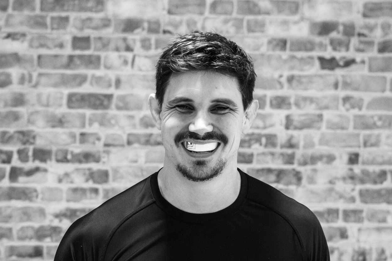 Man wearing a black 'Legacy' gumshield in front of a brick wall